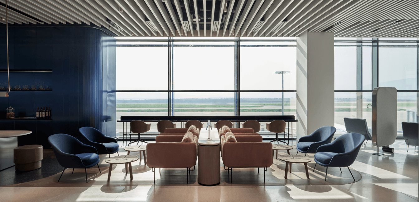 Χώρος business lounge, με καρέκλες και παράθυρα με θέα προς τον αεροδιάδρομο