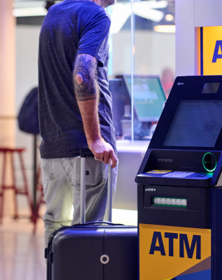 Person with baggage standing next to ATM in Athens International Airport